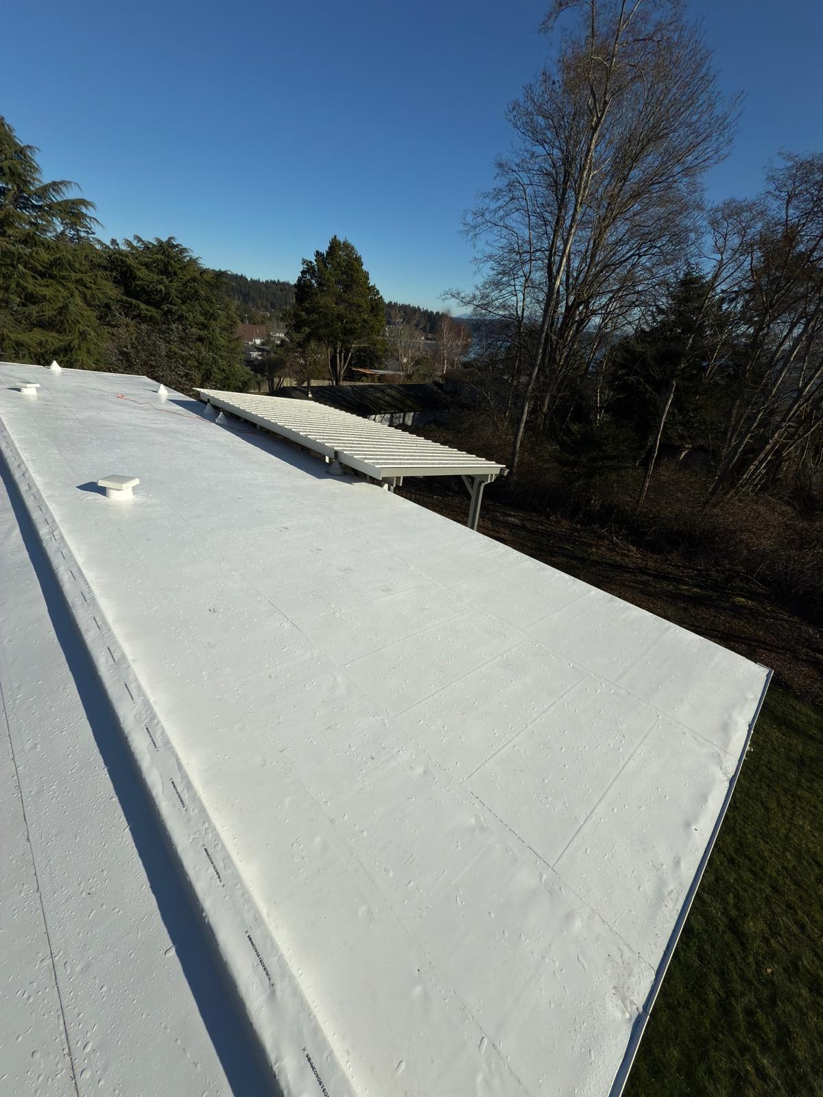 Completed white PVC low-slope roof beside evergreen trees in Anacortes, Washington