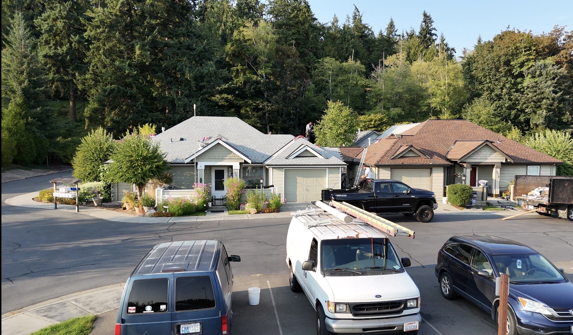 Roofing crew working on adjacent Maple Ridge homes with vehicles and materials staged nearby