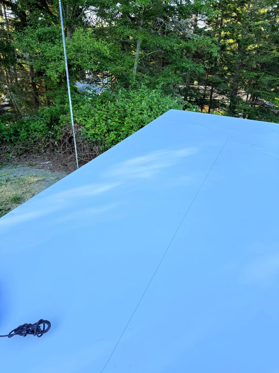 Completed white roof membrane and perimeter edge with trees beyond