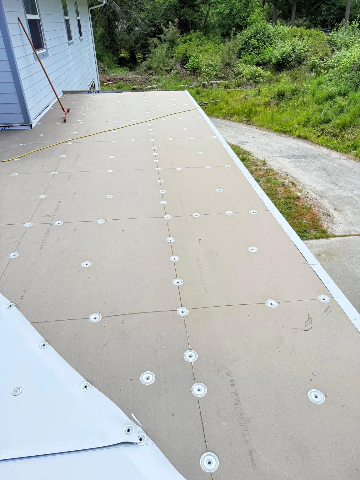 Secured roof panels and a partially rolled white membrane beside the house