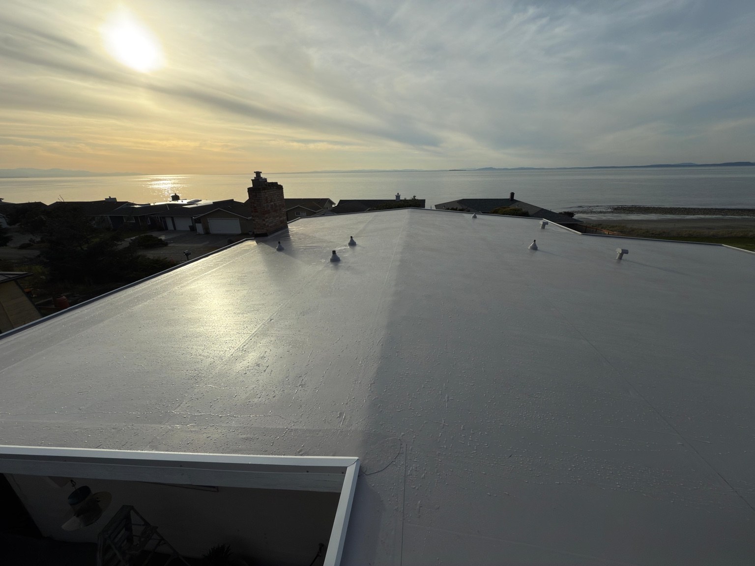 Wide view of the finished gray PVC roof and chimney with sunlight over the water