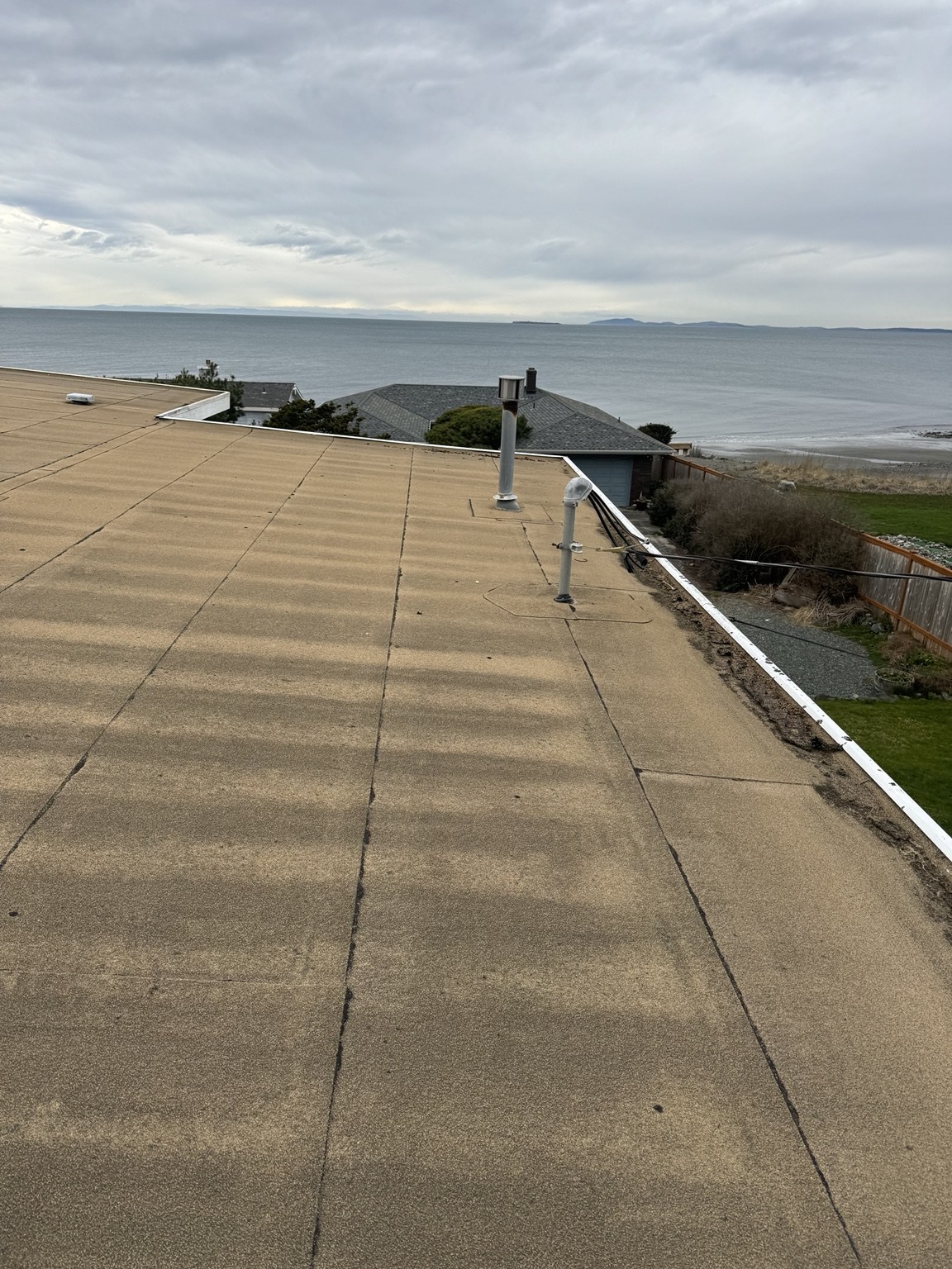 Old low-slope roof and pipe penetrations overlooking the water at West Beach